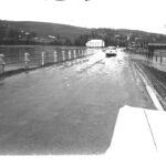 A 1960's car crossing some water flowing over a road.