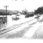 A large field submerged in water. Water is lapping onto the road for the length of the photograph.