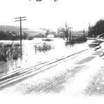 Photo is taking from a road looking out at a flooded field. Water level is high enough that it will soon submerge the road.