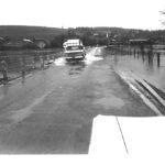 A 1950's pick-up truck crossing water flowing across a road. Water is deep enough that it is not very safe for the truck to cross. Grantsville, Maryland is in the background.