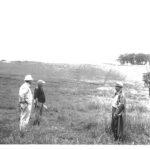 Three men stand in a field looking at the area.
