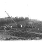 A crane and several bulldozers working in a field. Construction of the Winters' Dam, Oakland, Maryland.