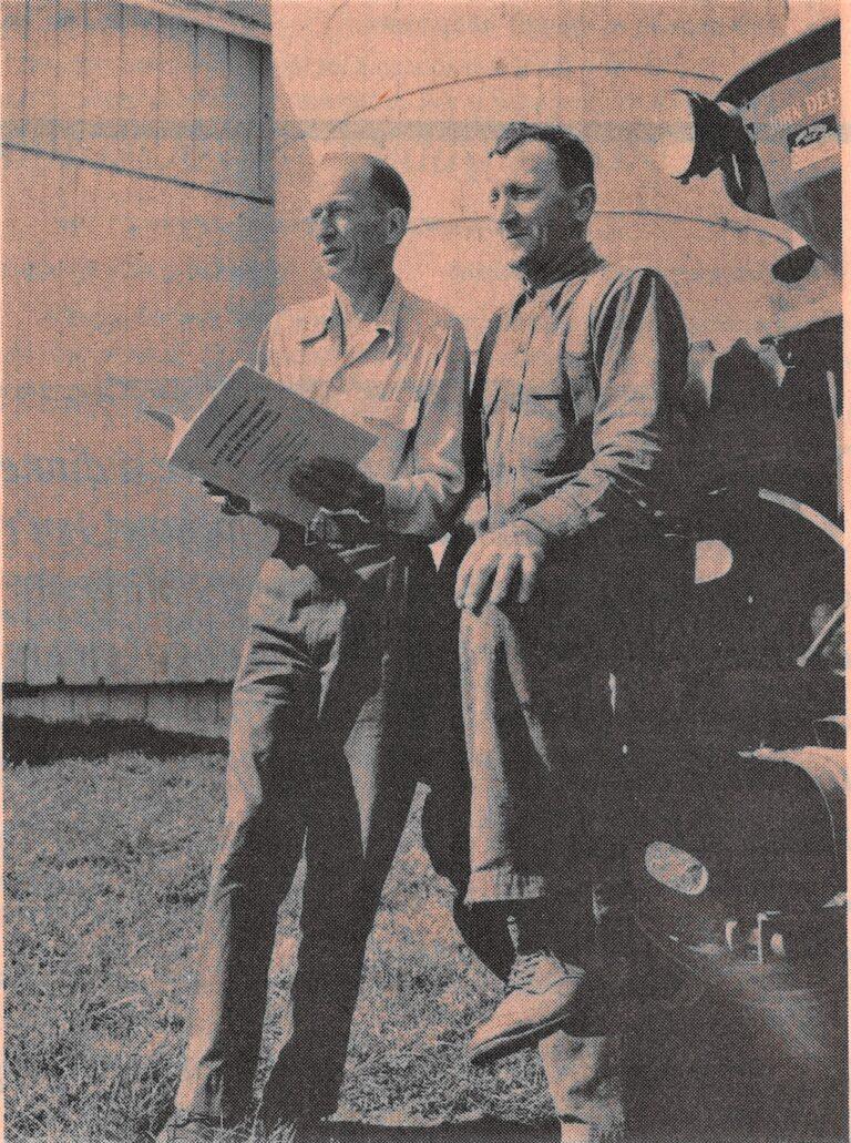 Two men leaning on a tractor holding a conservation book