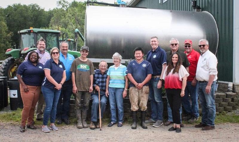 Maryland Secretary of Agriculture Kevin Atticks and staff pose in front of a milk tank, along with the owners and staff of a dairy farm.
