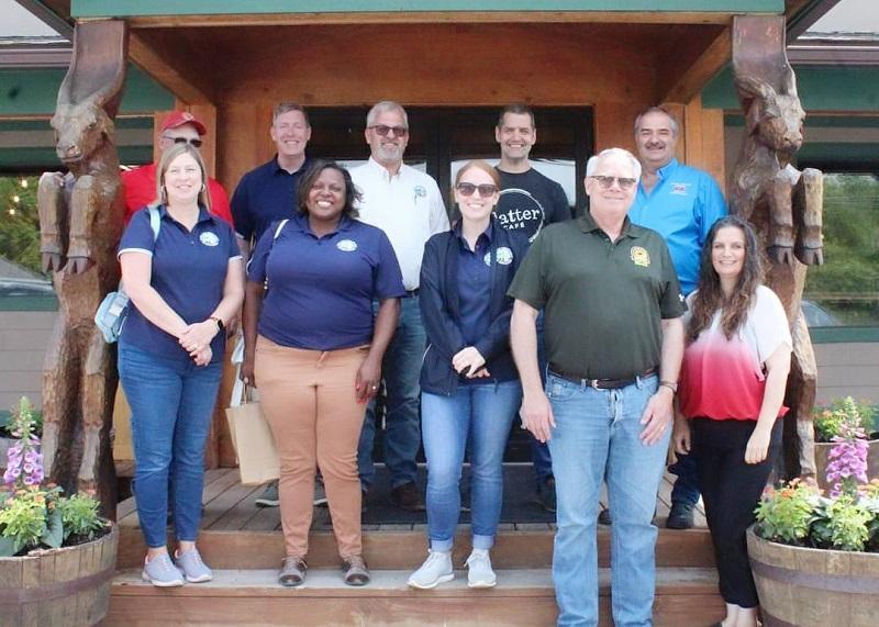 Secretary of Maryland Department of Agriculture Kevin Atticks and staff pose on the porch of a market with carved goat statues holding up the porch roof.