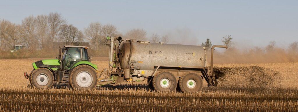 Green John Deere tractor pulling a manure tank that is spraying manure on a field.