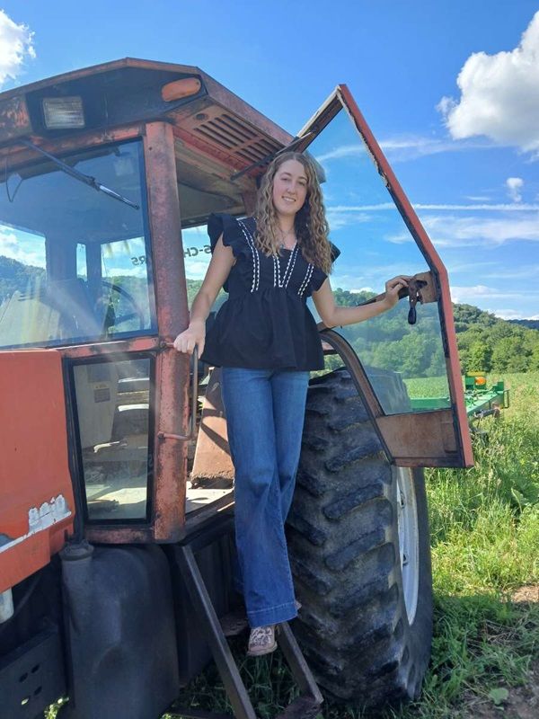 Cristy Enlow climbing down from her red cab-enclosed tractor.