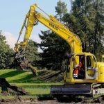 A yellow backhoe digging next to a pile of soil.